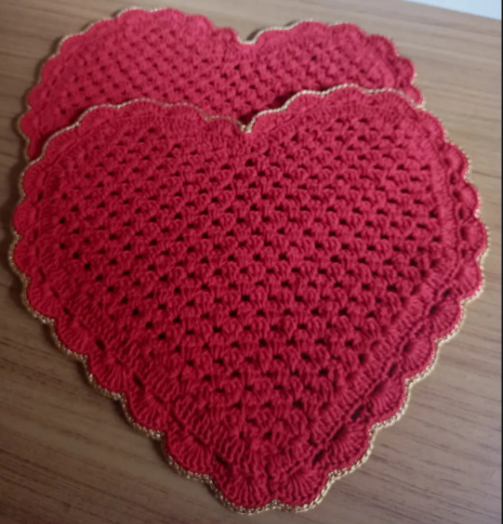 Corações de crochê vermelho, com borda dourada ondulada, sobre uma mesa de madeira.