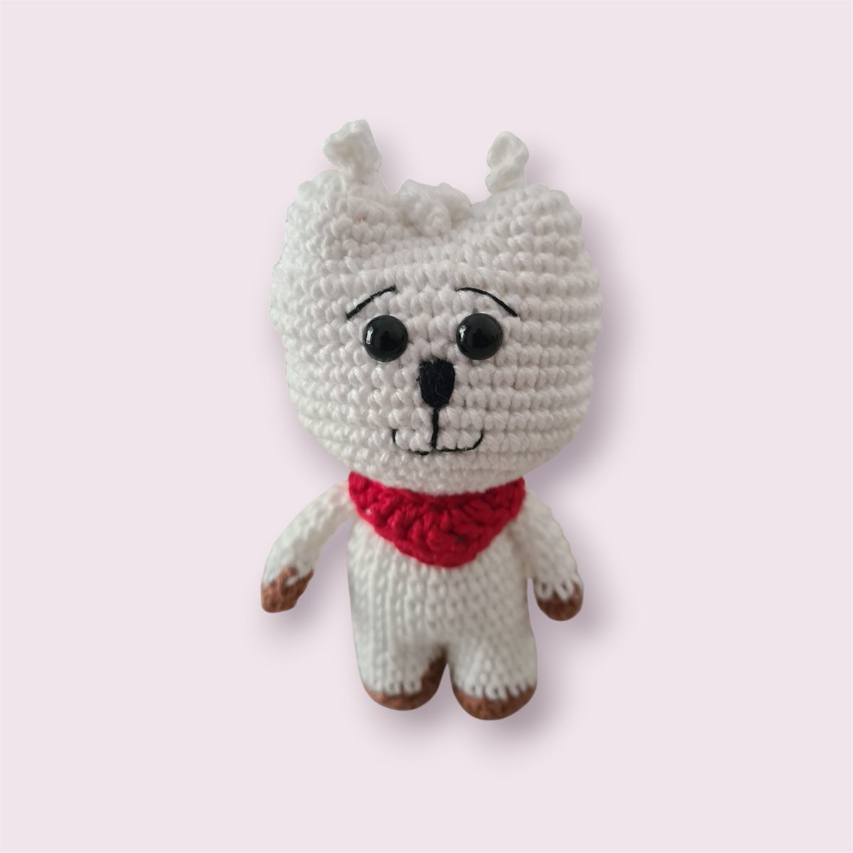 Amigurumi branco de crochê com cachecol vermelho, olhos pretos e patas marrons.