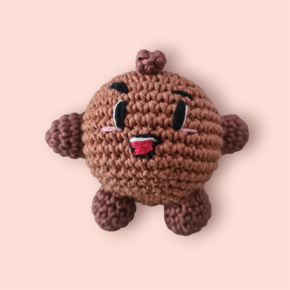 Amigurumi marrom de crochê em formato de bolinho, com boquinha aberta.