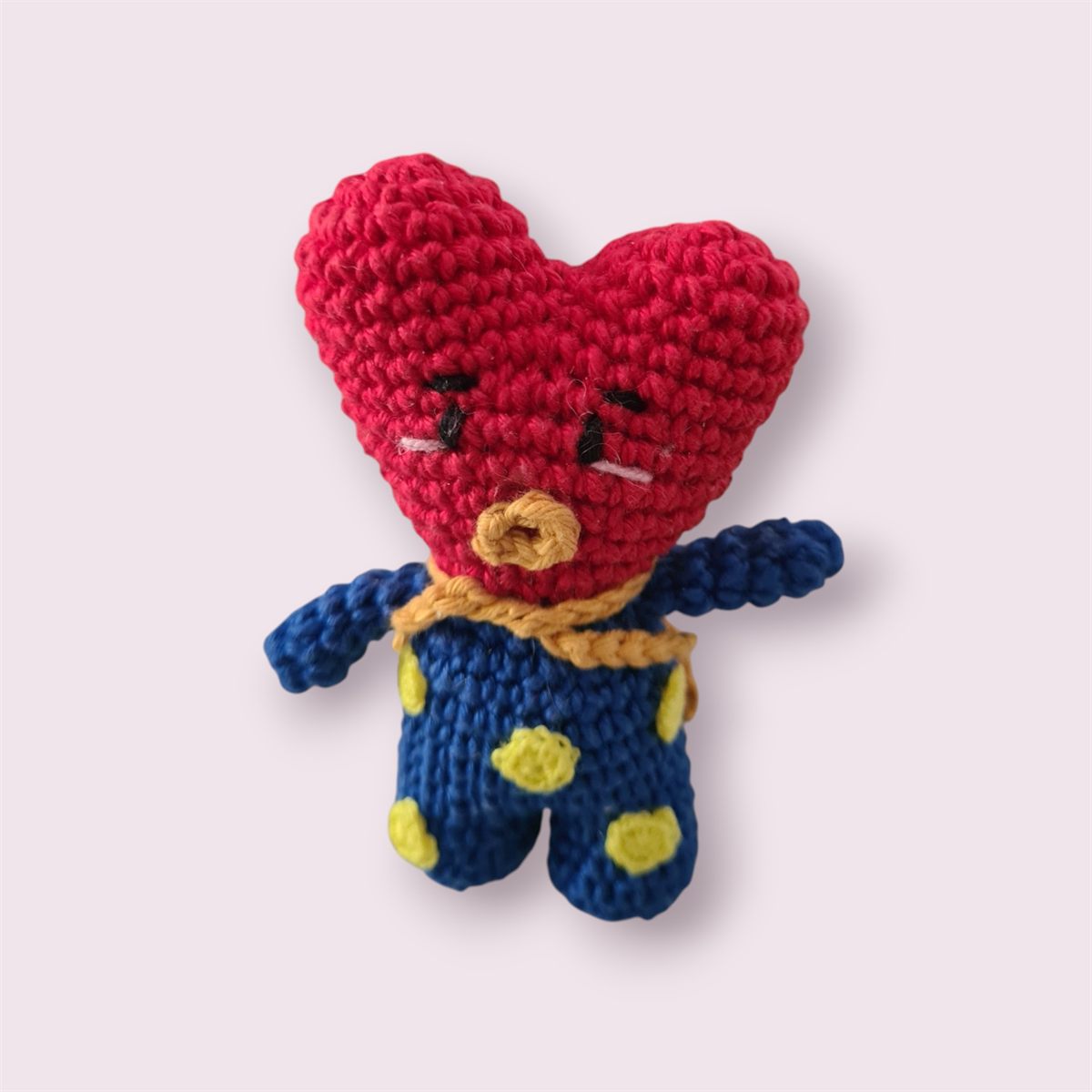Amigurumi em formato de coração vermelho, de macacão azul com bolinhas amarelas.